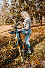 Plakat Woman on yellow Bicycle walking in the autumn Park. Middle-aged woman