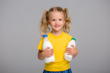 little blonde girl in a yellow t-shirt holding plastic bottles of milk, smiling and looking into the frame, space for text