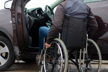 A man in a wheelchair trying to get into the driver's seat of a car