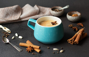 Fototapeta na wymiar Indian masala chai tea, traditional spiced black tea with milk in blue cup on dark background