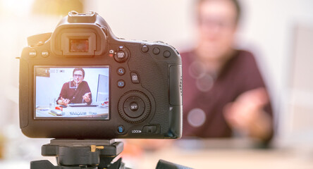 Video blogger at home: Camera on tripod is filming a young man sitting on his working place