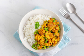 Rice and Cauliflower Curry with Green Peas in a Bowl Garnished with Cilantro Top View Photo on White Background..