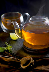 Hot tea in glass teapot and cup with steam on wood background