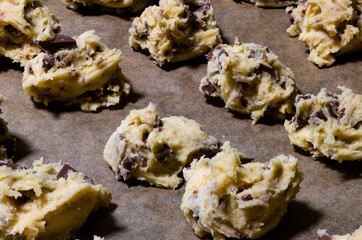 Raw chocolate cookie dough. Portions of dough with chocolate pieces arranged in rows lying on baking paper. Bakery background.