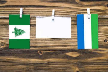 Hanging flags of Norfolk Island and Sierra Leone attached to rope with clothes pins with copy space...