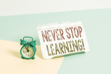 Word writing text Never Stop Learning. Business photo showcasing keep on studying gaining new knowledge or materials Mini size alarm clock beside a Paper sheet placed tilted on pastel backdrop