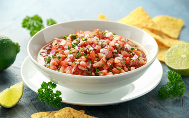 Mexican Tomato Salsa in white bowl with lime, red onion, jalapeno pepper, parsley and tortilla chips