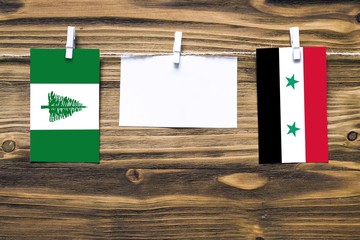 Hanging flags of Norfolk Island and Syria attached to rope with clothes pins with copy space on...