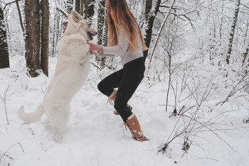 young woman jumping in the snow with a dog 