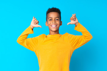 African American boy over isolated blue background proud and self-satisfied - obrazy, fototapety, plakaty