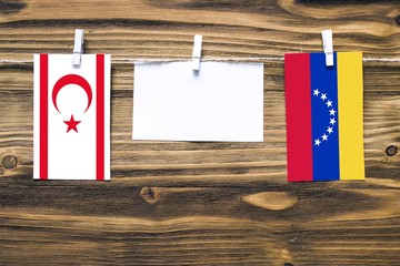 Hanging flags of Northern Cyprus and Venezuela attached to rope with clothes pins with copy space on white note paper on wooden background.Diplomatic relations between countries.