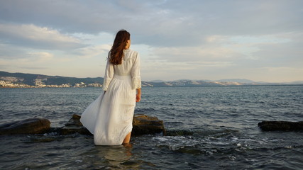 Fototapeta na wymiar Woman Wearing White Long Dress And Standing In The Sea