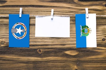 Hanging flags of Northern Mariana Islands and San Marino attached to rope with clothes pins with copy space on white note paper on wooden background.Diplomatic relations between countries.