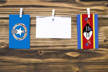 Hanging flags of Northern Mariana Islands and Swaziland attached to rope with clothes pins with copy space on white note paper on wooden background.Diplomatic relations between countries.