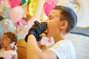 Obraz na płótnie Canvas The handsome little boy eating burger in black rubber gloves.