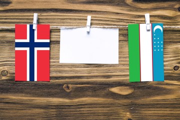 Hanging flags of Norway and Uzbekistan attached to rope with clothes pins with copy space on white note paper on wooden background.Diplomatic relations between countries.