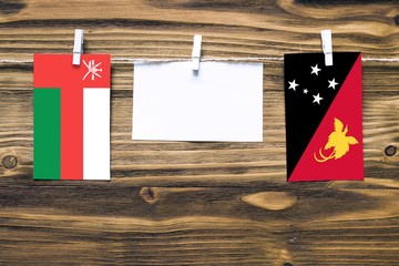 Hanging flags of Oman and Papua New Guinea attached to rope with clothes pins with copy space on white note paper on wooden background.Diplomatic relations between countries.