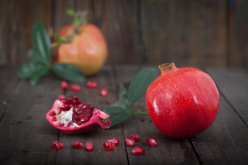 Fresh pomegranates with leaves on wooden background.Two ripe, juicy pomegranates, one cut.