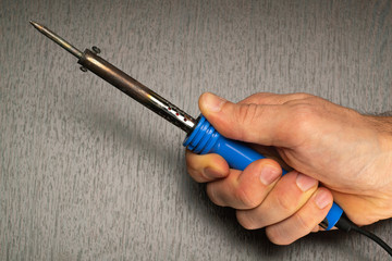 Soldering iron in hand, close-up on a dark background