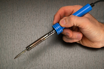 Soldering iron in hand, close-up on a dark background