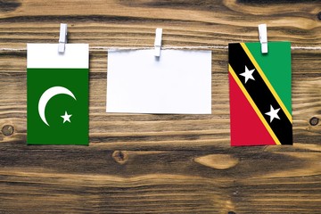 Hanging flags of Pakistan and Saint Kitts And Nevis attached to rope with clothes pins with copy space on white note paper on wooden background.Diplomatic relations between countries.