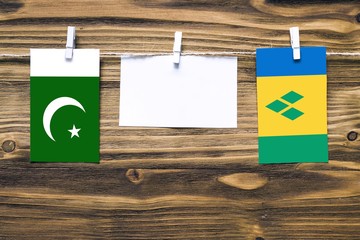 Hanging flags of Pakistan and Saint Vincent And The Grenadines attached to rope with clothes pins with copy space on white note paper on wooden background.Diplomatic relations between countries.