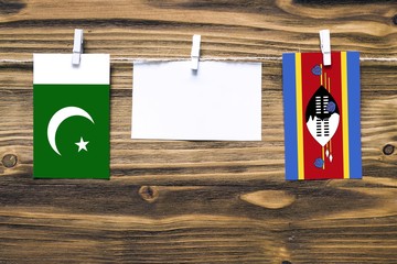 Hanging flags of Pakistan and Swaziland attached to rope with clothes pins with copy space on white note paper on wooden background.Diplomatic relations between countries.
