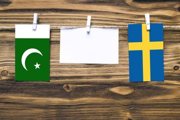 Hanging flags of Pakistan and Sweden attached to rope with clothes pins with copy space on white note paper on wooden background.Diplomatic relations between countries.