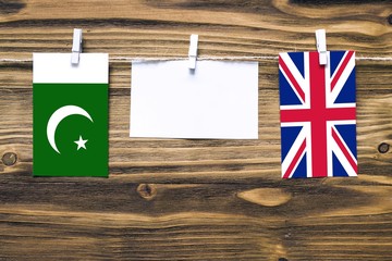 Hanging flags of Pakistan and United Kingdom attached to rope with clothes pins with copy space on white note paper on wooden background.Diplomatic relations between countries.