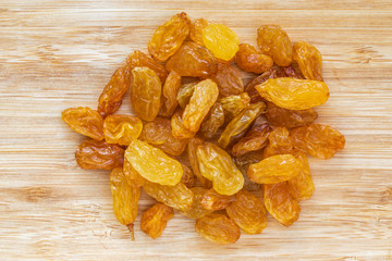 A pile of raisins lies in the center on a brown wooden surface, top view