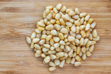 Pine nuts lie in a heap in the center on a brown wooden surface, top view