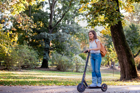 Young woman in jeans  riding electric scooter through the park