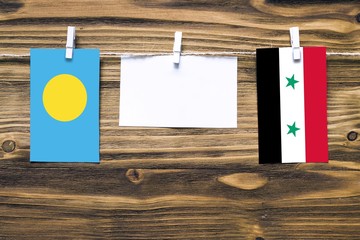 Hanging flags of Palau and Syria attached to rope with clothes pins with copy space on white note paper on wooden background.Diplomatic relations between countries.