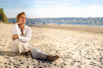 Fototapeta na wymiar Elegant woman in white robes with turban sitting on the beach