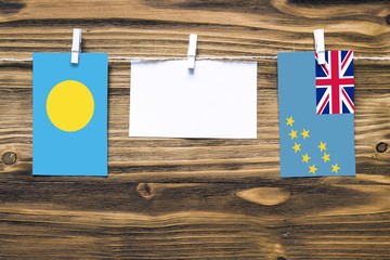 Hanging flags of Palau and Tuvalu attached to rope with clothes pins with copy space on white note paper on wooden background.Diplomatic relations between countries.