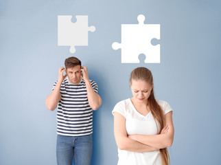 Young quarrelled couple and pieces of puzzle on blue background