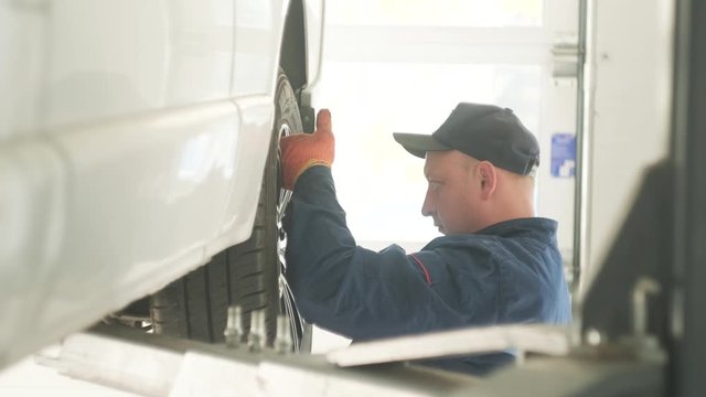 expert specialist technician changes tires, tyres of lifted up car, at auto workshop