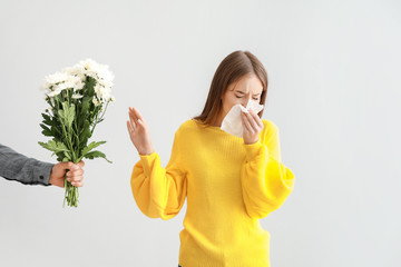 Young woman with allergy refusing to take flowers from man on light background