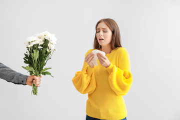 Man giving flowers to young woman suffering from allergy on light background - obrazy, fototapety, plakaty