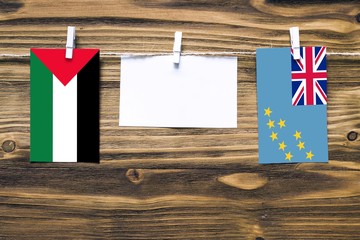 Hanging flags of Palestine and Tuvalu attached to rope with clothes pins with copy space on white note paper on wooden background.Diplomatic relations between countries.