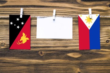 Hanging flags of Papua New Guinea and Philippines attached to rope with clothes pins with copy space on white note paper on wooden background.Diplomatic relations between countries.
