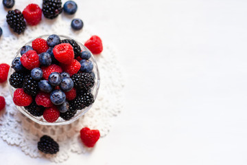 Ripe seasonal berries in glass bowl: raspberry, blueberry, blackberry. Healthy and no calories snack. White wooden background. Top view, flat lay, copy space for text