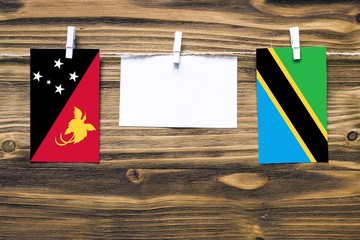 Hanging flags of Papua New Guinea and Tanzania attached to rope with clothes pins with copy space on white note paper on wooden background.Diplomatic relations between countries.
