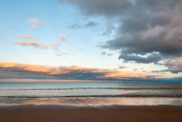 Dramatic sky over the sea as waves gently lap onto the beach in the golden light of the setting sun