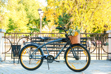Fototapeta premium Modern bicycle with basket and bouquet of flowers on city street
