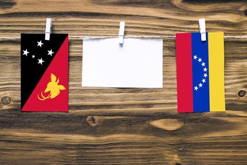 Hanging flags of Papua New Guinea and Venezuela attached to rope with clothes pins with copy space on white note paper on wooden background.Diplomatic relations between countries.