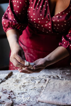 Woman in red dress and apron is preparing a dough for delicious homemade pink pasta on her kitchen. Dark and moody, low key. Flour all over