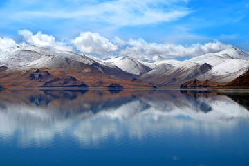Fototapeta na wymiar The Yamdrok Lake, reflecting the brown colors of Mt. Naiqinkangsang against a blue clear sky.