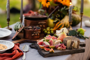 Beautiful autumn composition with two copper pans. Dark wooden board with delicious italian food: cheese, meat, fresh fruits. Pumpkins and flowers as decor
