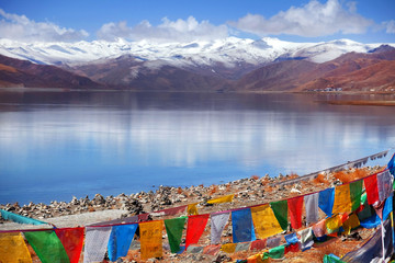Tibetan praying flags in front of the Yamdrok Lake, reflecting the brown colors of Mt....